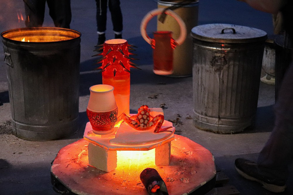 Pieces get moved from the kiln base to nearby metal garbage cans with reduction materials inside.

PHOTO CREDIT: Ella Spillman